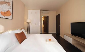 A hotel room with a bed, a TV, a wardrobe, and a door leading to another room.