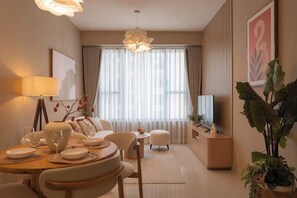 A modern living room with a dining area, a sofa, a television, and a large window with curtains. - 2BR + 2BA • 3 Beds • Group-Friendly • Central • D1 (Ho Chi Minh City)