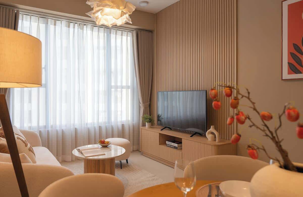 Ein modernes Wohnzimmer mit Flachbildfernseher, einer Couch, einem Couchtisch und einem Esstisch mit einem Weinglas.