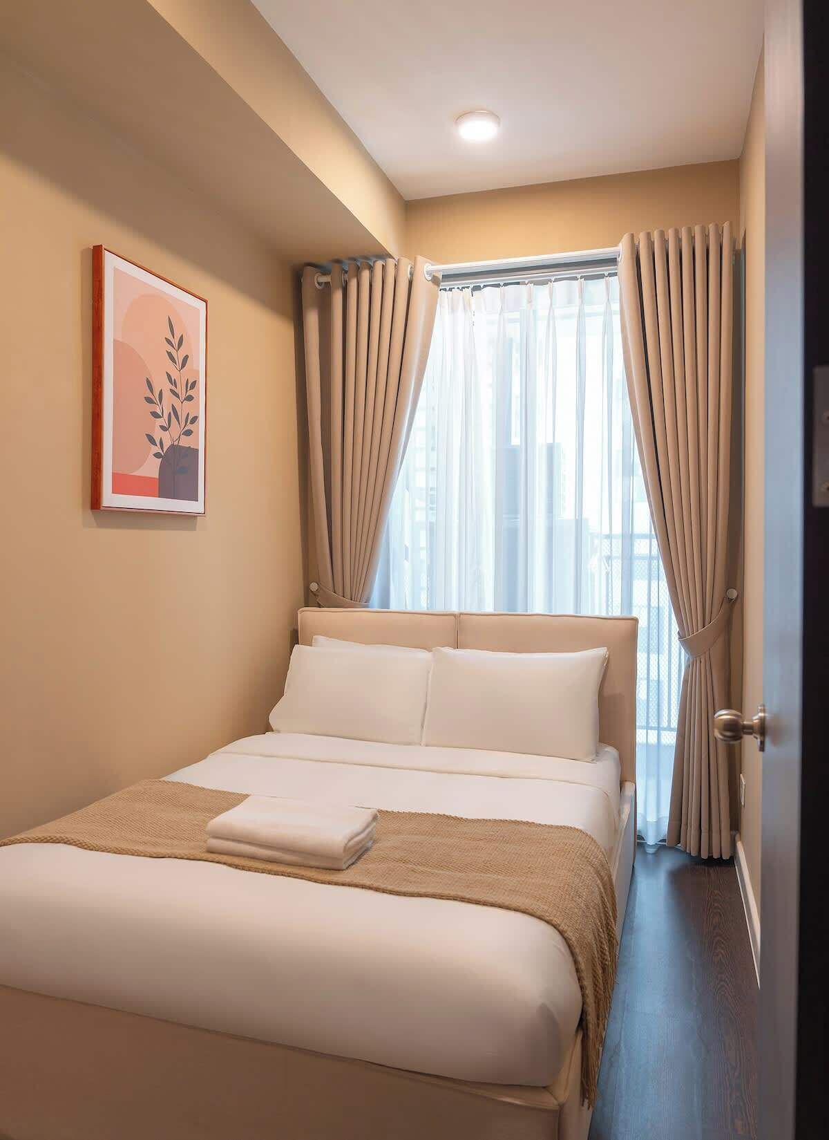 Een hotelkamer met een bed, gordijnen, een raam en een lijst met een afbeelding aan de muur.