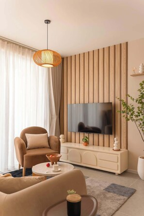 A modern living room with a flat-screen TV mounted on a wooden panel wall, a comfortable sofa, a coffee table with decorative items, and a hanging light fixture. - Stunning 3BR+2BA Apt w/View | Near Bui Vien & D1 (Thành phố Hồ Chí Minh)