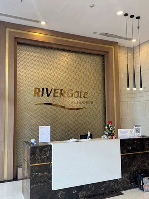 A reception desk with a marble counter, a wall-mounted sign reading 'RIVERGate,' and a small Christmas tree decoration. - Stunning 3BR+2BA Apt w/View | Near Bui Vien & D1 (Thành phố Hồ Chí Minh)