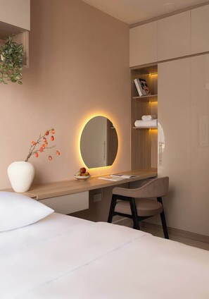 Ett modernt hotellrum med en säng, ett skrivbord med en spegel, en stol och en garderob.