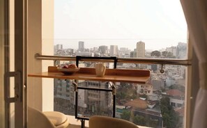 A room with a view of a cityscape through a window, a metal shelf with a bowl and a vase, and a chair. - Warm Central 2BR+1Bath | D3, City View, Pool, Gym (Võ Thị Sáu)
