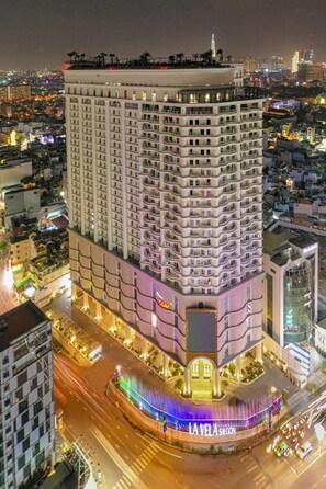 A multi-story hotel with a curved facade, a prominent entrance, and a view of the surrounding cityscape at night. - Warm Central 2BR+1Bath | D3, City View, Pool, Gym (Võ Thị Sáu)