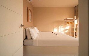 A hotel room with a bed, a wardrobe, a shelf with towels, and a framed picture on the wall. - Warm Central 2BR+1Bath | D3, City View, Pool, Gym (Võ Thị Sáu)