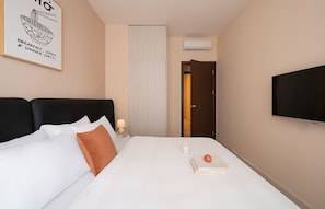A hotel room with a bed, a flat-screen TV, a wall-mounted air conditioner, and a door leading to another room. - Luxe 2BR+1BA | Central, 2 min BuiVien | D1, Tresor (Thành phố Hồ Chí Minh)
