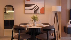 Uma sala de jantar com uma mesa redonda, seis cadeiras, um vaso com flores e um lustre.
