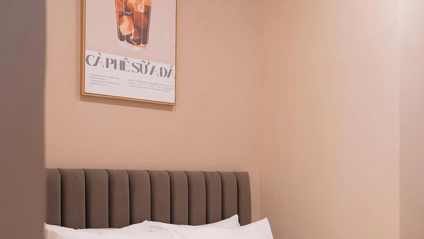 Uma cama bem arrumada com lençóis brancos e cabeceira marrom, um quadro na parede e uma maçã vermelha sobre a cama.