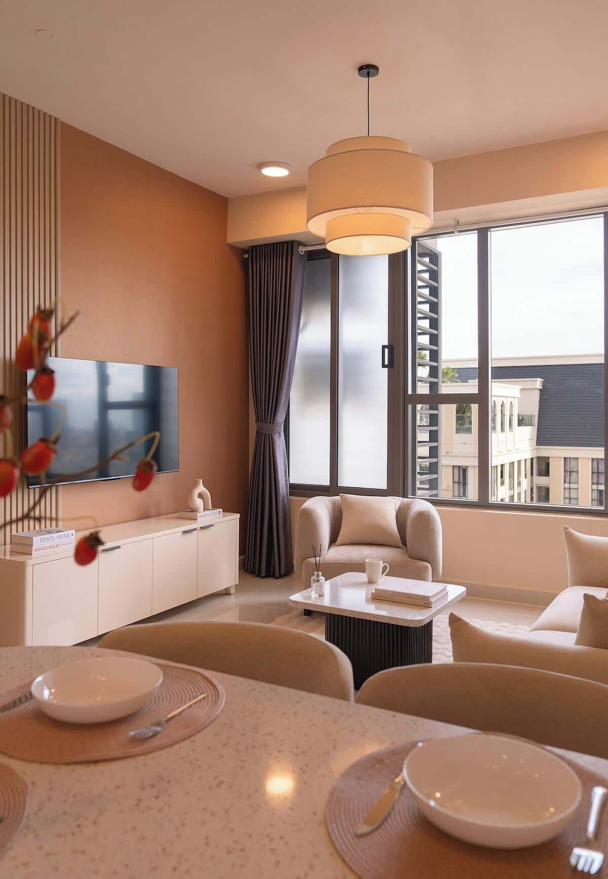Et moderne hotelværelse med et stort vindue, et fladskærms-tv, en sofa, et spisebord med tallerkener og bestik samt en dekorativ vase med røde bær.
