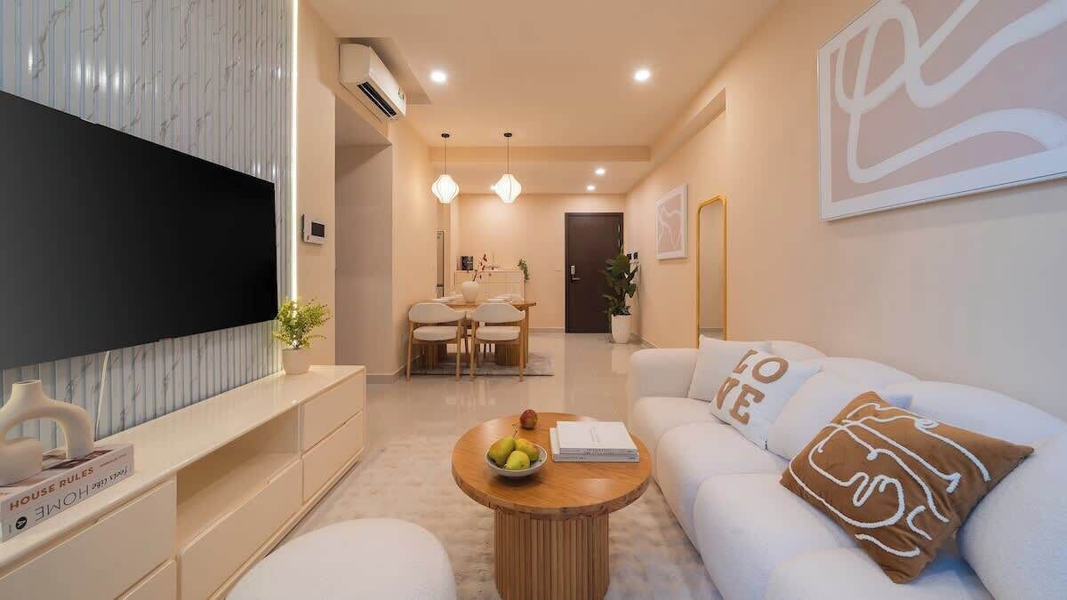 Ein modernes Wohnzimmer mit Flachbildfernseher, Essbereich mit Tisch und Stühlen sowie Sofa mit dekorativen Kissen.