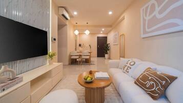 Ein modernes Wohnzimmer mit Flachbildfernseher, Essbereich mit Tisch und Stühlen sowie Sofa mit dekorativen Kissen.