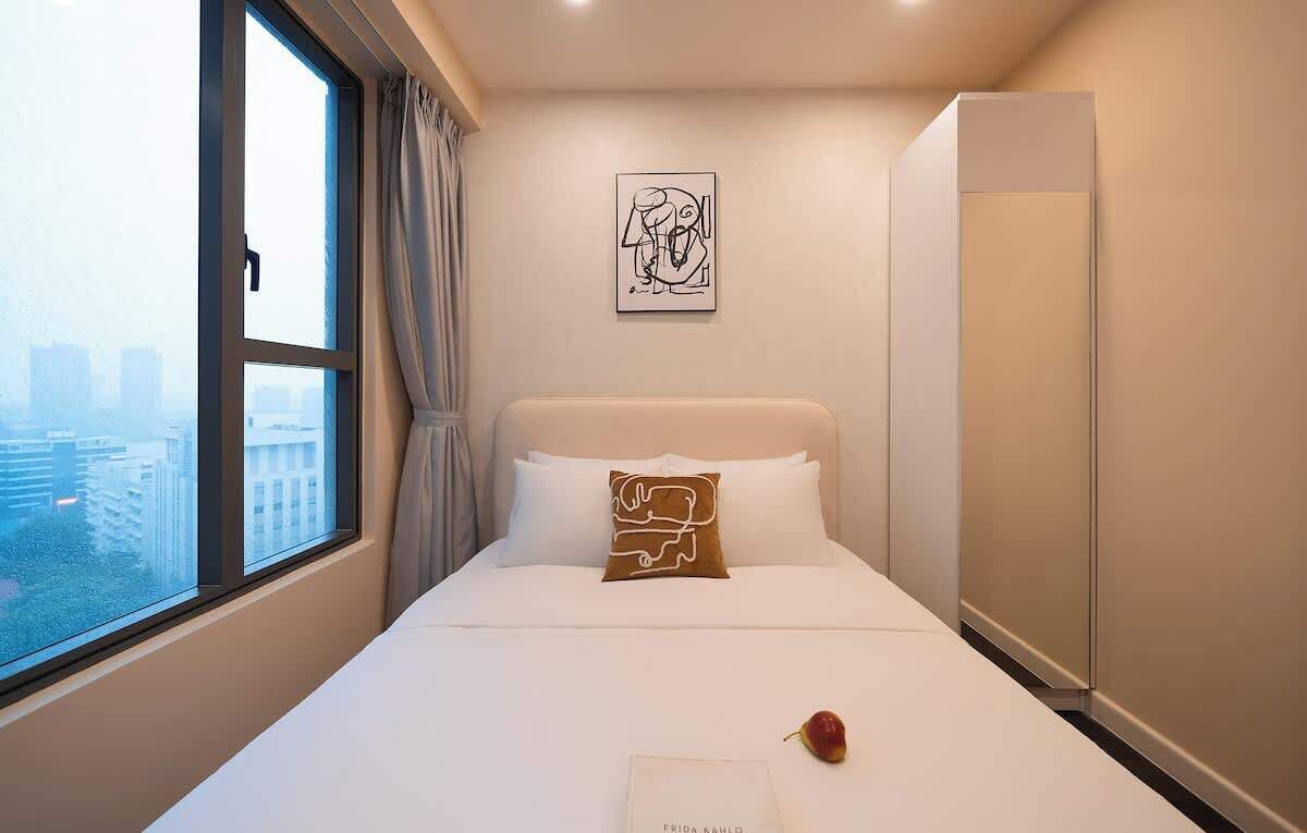 Ein Hotelzimmer mit Bett, Fenster mit Vorhängen, Blick auf die Stadt, Wandkunst und einem Kleiderschrank.