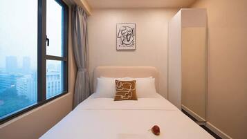 Ein Hotelzimmer mit Bett, Fenster mit Vorhängen, Blick auf die Stadt, Wandkunst und einem Kleiderschrank.