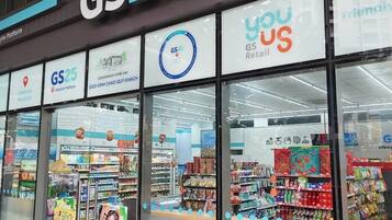 Un magasin GS25, de type épicerie de proximité, avec une façade en verre transparent, différents présentoirs de produits et des affiches promotionnelles.