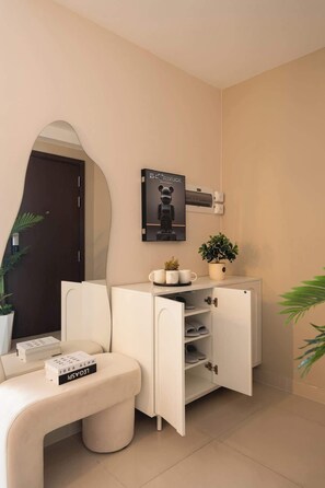 A modern, minimalist room with a white sofa, a small side table, a white cabinet with open shelves, a potted plant, and a framed picture on the wall. - 3BR | 2BA • Near D1 • River View • Dryer • HighFLR (Thành phố Hồ Chí Minh)