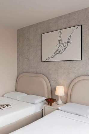Una habitación de hotel con dos camas, una mesita de noche con lámpara y una obra de arte en la pared.