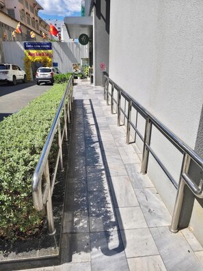 Ein Bürgersteig mit Metallgeländern, ein Gebäude mit einem Schild und ein Auto, das am Straßenrand geparkt ist.