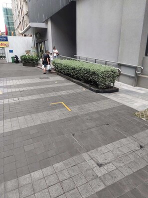 Un espacio al aire libre empedrado con barandilla de metal, un seto y un edificio al fondo.