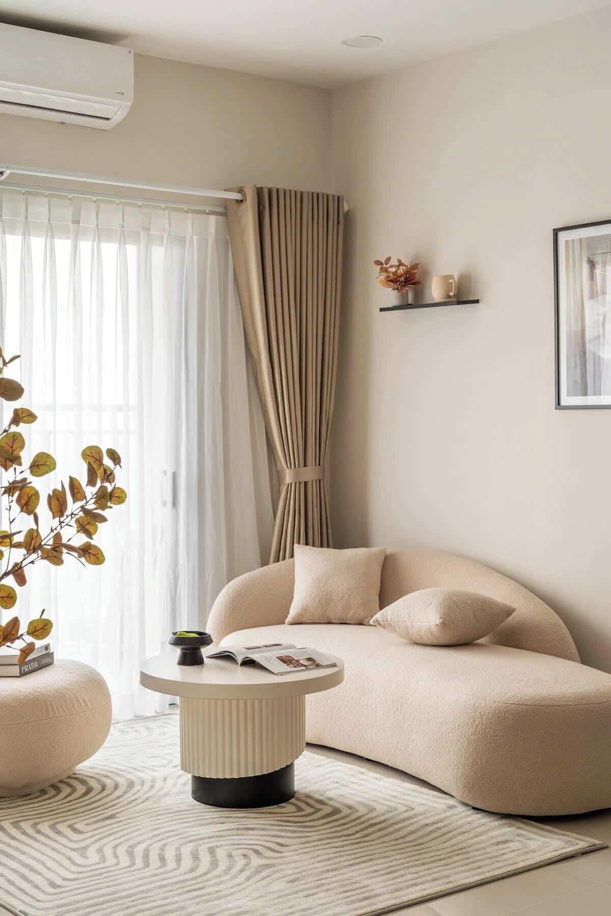 Una sala de estar moderna con un sofá color beige, una mesa de centro redonda y un gran ventanal con cortinas traslúcidas.