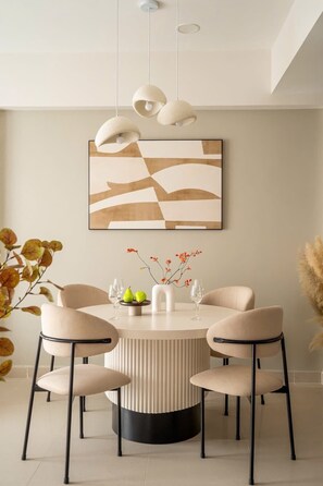 A dining area with a round table, four chairs, a vase with flowers, and a wall-mounted abstract painting. - 2BR + 3 Beds | 1BA • Central D1 • Side River View (Thành phố Hồ Chí Minh)
