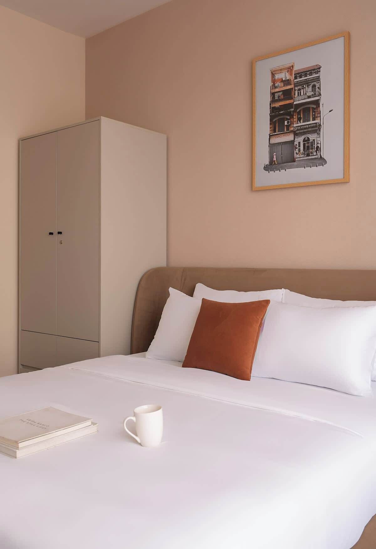 Hotelkamer met een bed, een kledingkast, een lijst aan de muur, een boek en een kopje.