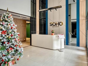 Un mostrador de recepción con un árbol de Navidad a la izquierda, un cartel que dice 'SOHO RESIDENCE' en la pared y una pequeña planta sobre el mostrador.