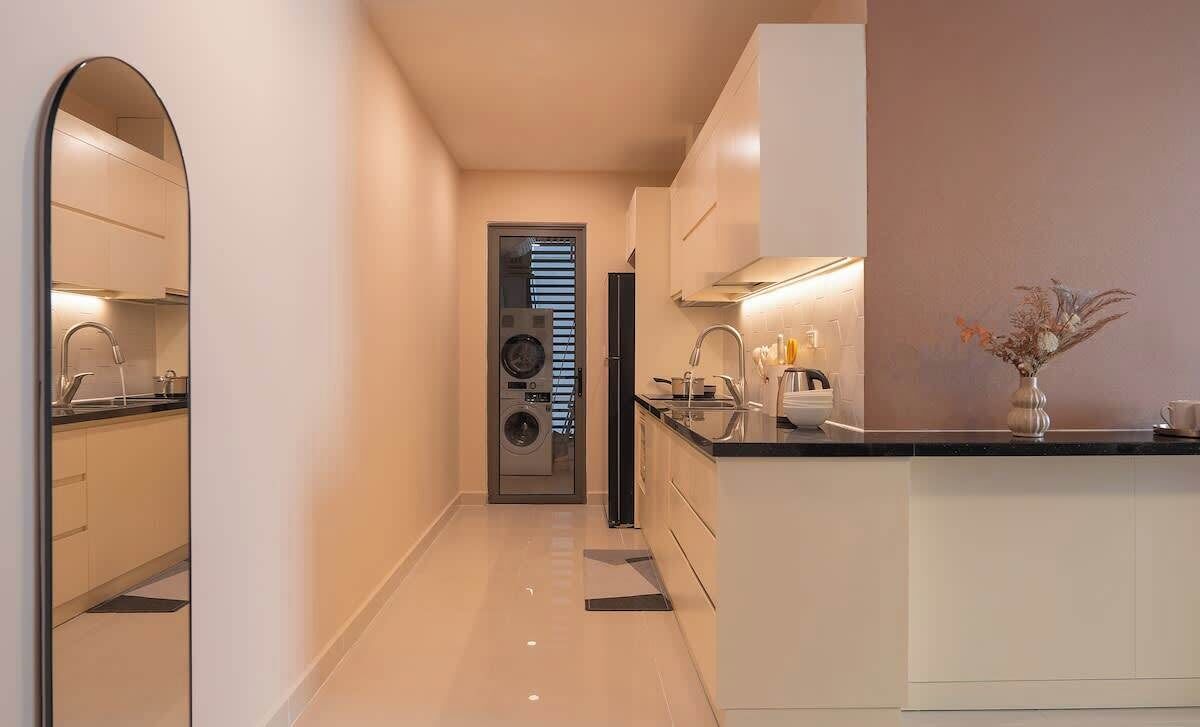 Une cuisine moderne avec un îlot central, un four encastré et un lave-linge à l’arrière-plan.