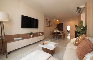 Ein modernes Wohnzimmer mit Flachbildfernseher, einem Essbereich und einer Küche im Hintergrund.