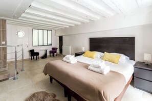 A hotel room with a large bed, a round mirror, a small table, two chairs, a nightstand with a lamp, and a radiator. - Charming apartment in the heart of le marais (Paris)