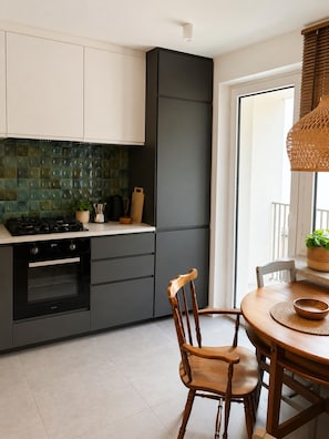A modern kitchen with a gas stove, oven, and a dining area with a wooden table and chairs. - Native Apartments Starowiślna 25 (Kraków)