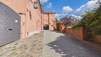 A cobblestone street leading to a building with a large metal gate and a brick wall on the right.