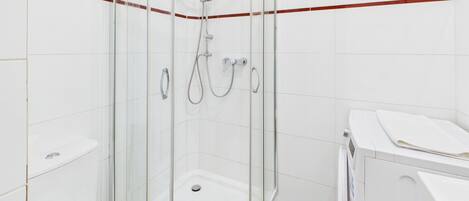 Ducha con puerta de vidrio, tina blanca y inodoro blanco.