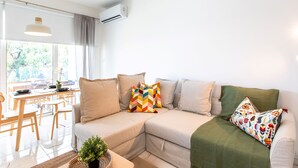 A modern living room with a sectional sofa, a dining table, and a potted plant. - Platinum Breeze - 1-BR Apt. in Larnaca (Larnaka)