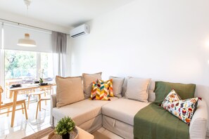 A modern living room with a sectional sofa, a dining table, and a potted plant. - Platinum Breeze - 1-BR Apt. in Larnaca (Larnaka)