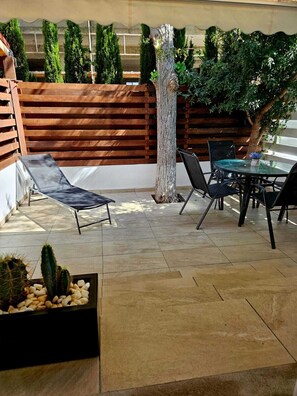 Eine Terrasse im Freien mit Tisch und Stühlen, einem Liegestuhl und einem Kaktus-Pflanzgefäß.
