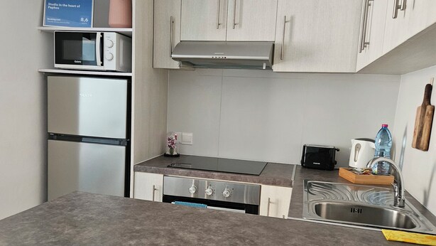 A modern kitchen with stainless steel appliances, a built-in oven, a microwave, and a sink. There is a bar stool and a decorative item on the counter. - Studio in the heart of Paphos (Pafos)