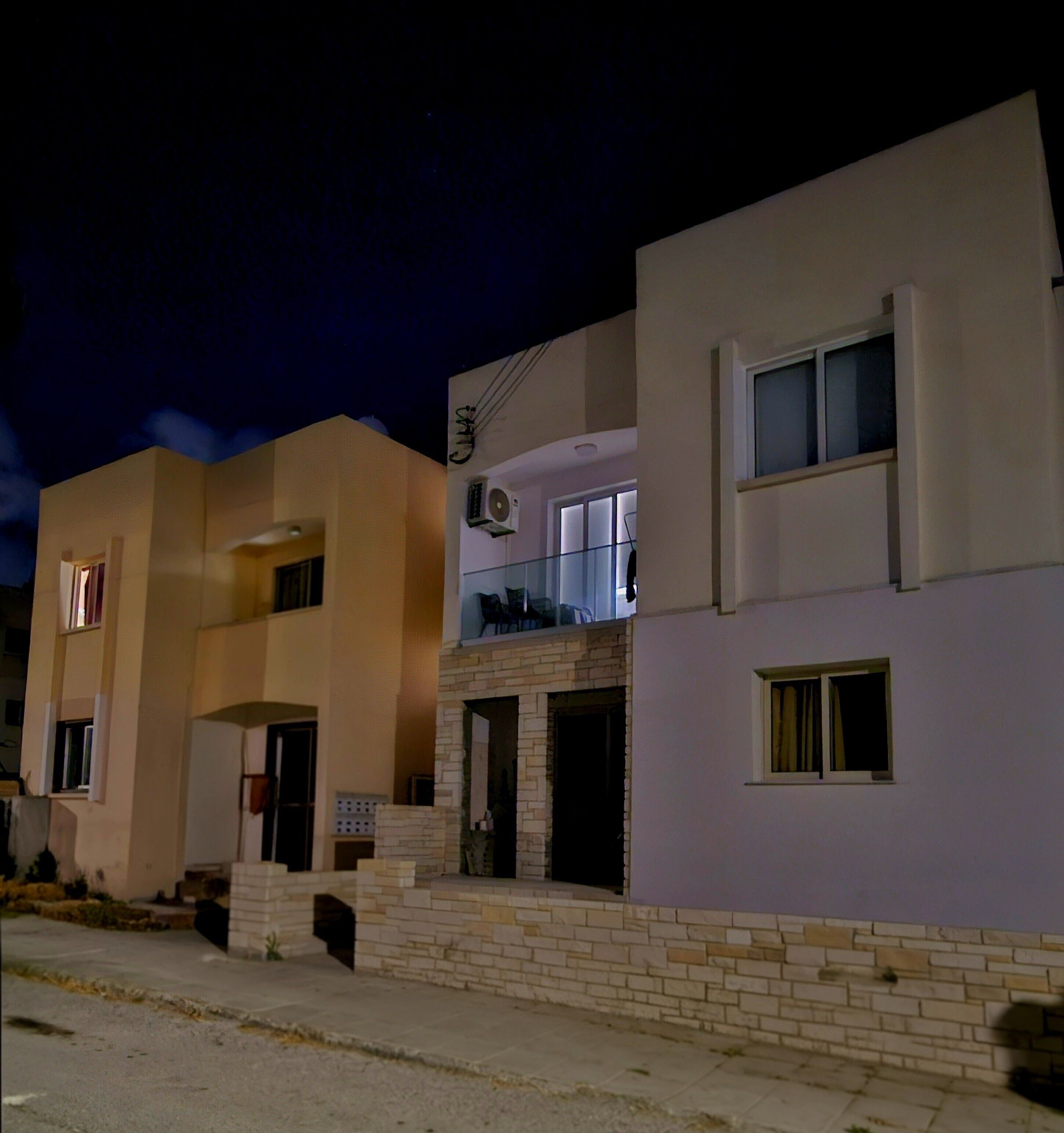 Un edificio residencial con fachada plana, entrada de ladrillo y un balcón con mobiliario exterior.