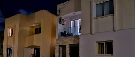 Un edificio residencial con fachada plana, entrada de ladrillo y un balcón con mobiliario exterior.