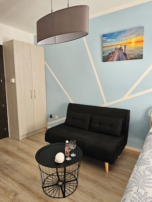 A modern room with a black sofa, a round black table with a white object, a pendant light, and a painting of a sunset on the wall. - Studio in the heart of Paphos (Pafos)
