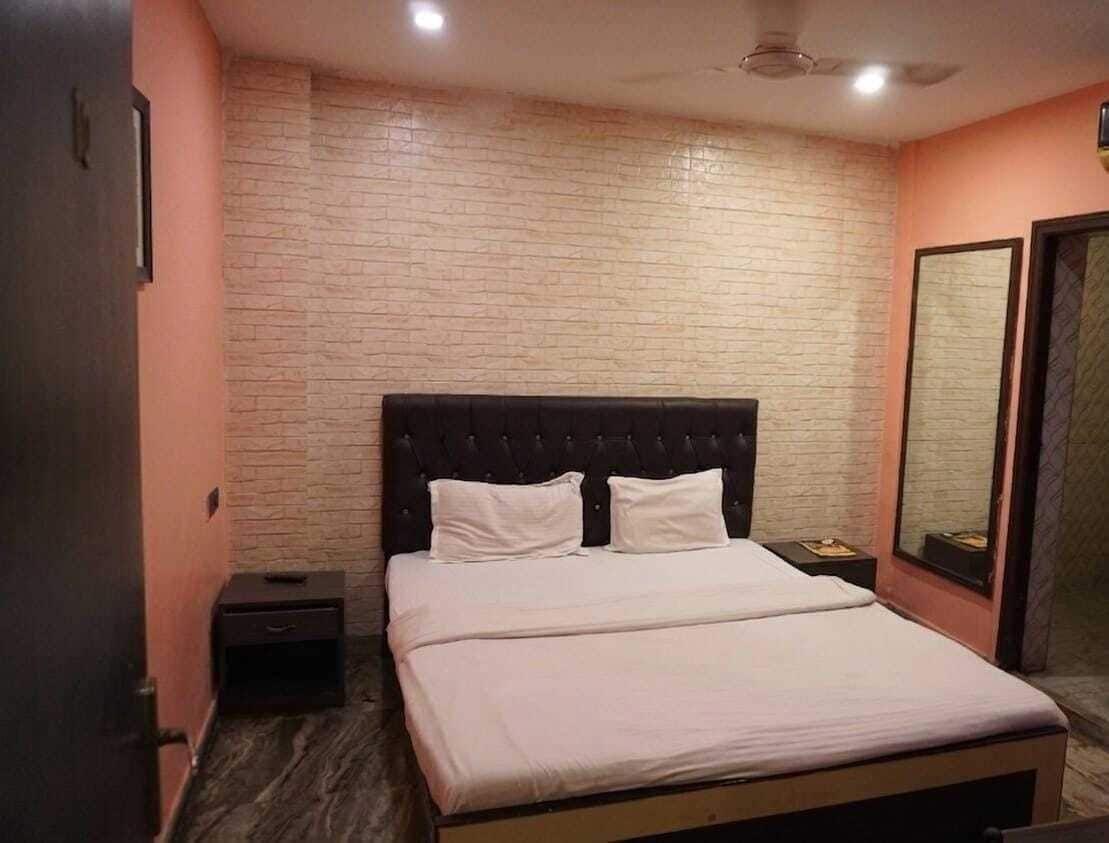 A bedroom with a brick-patterned wall, a bed with white bedding, a dark headboard, and a nightstand with a lamp.
