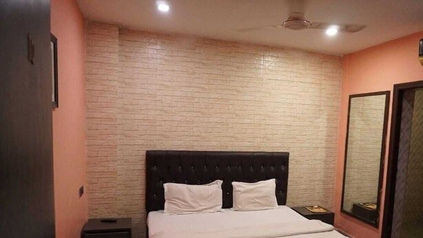 A bedroom with a brick-patterned wall, a bed with white bedding, a dark headboard, and a nightstand with a lamp. - Hotel Church View (Kolkata)