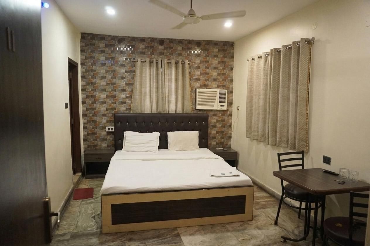 A hotel room with a bed, a bedside table, a chair, a small table, and a ceiling fan.