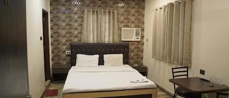 A hotel room with a bed, a bedside table, a chair, a small table, and a ceiling fan.