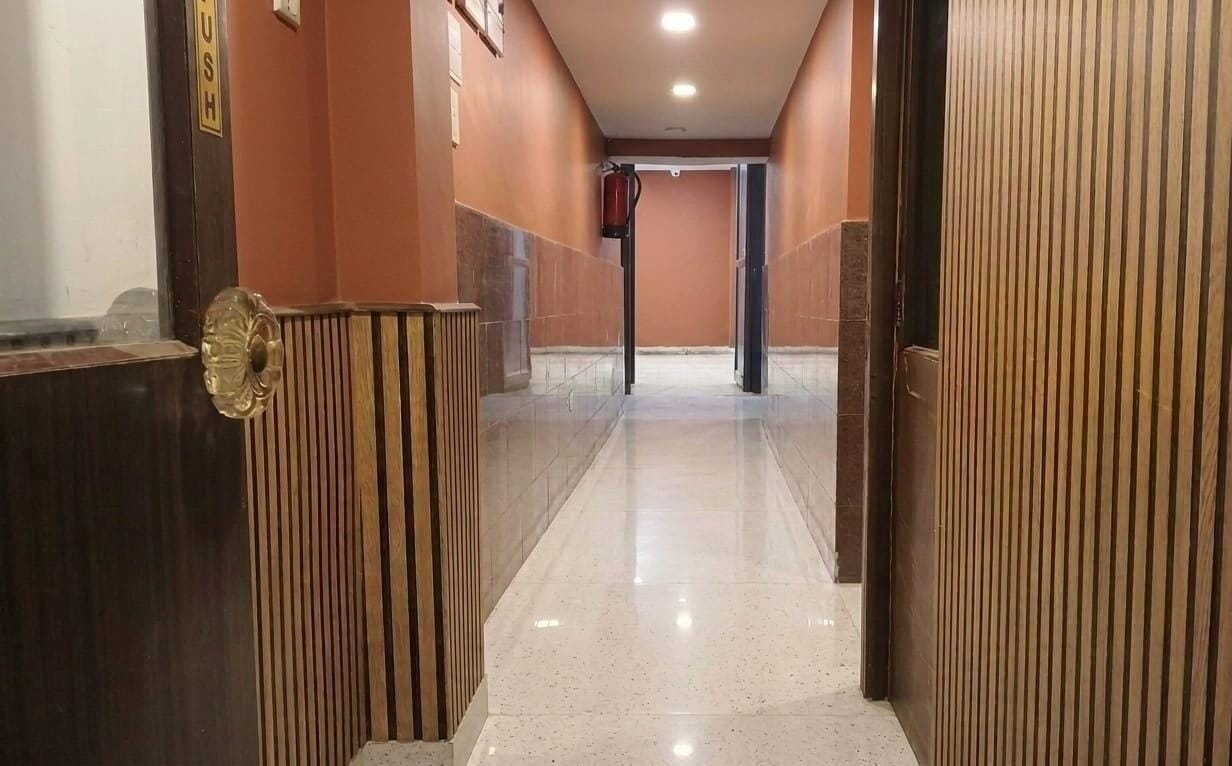 A corridor with a polished floor, wooden paneling on the walls, and a door with a brass handle.