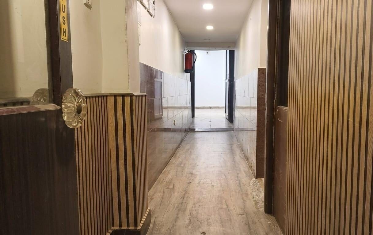 A hallway with a wooden floor, a door with a vertical stripe pattern, and a fire extinguisher mounted on the wall.