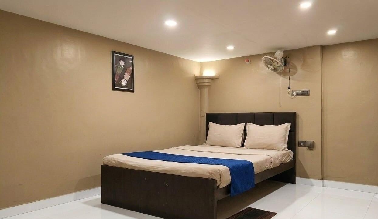 A bedroom with a bed, a wall-mounted fan, and a picture on the wall.