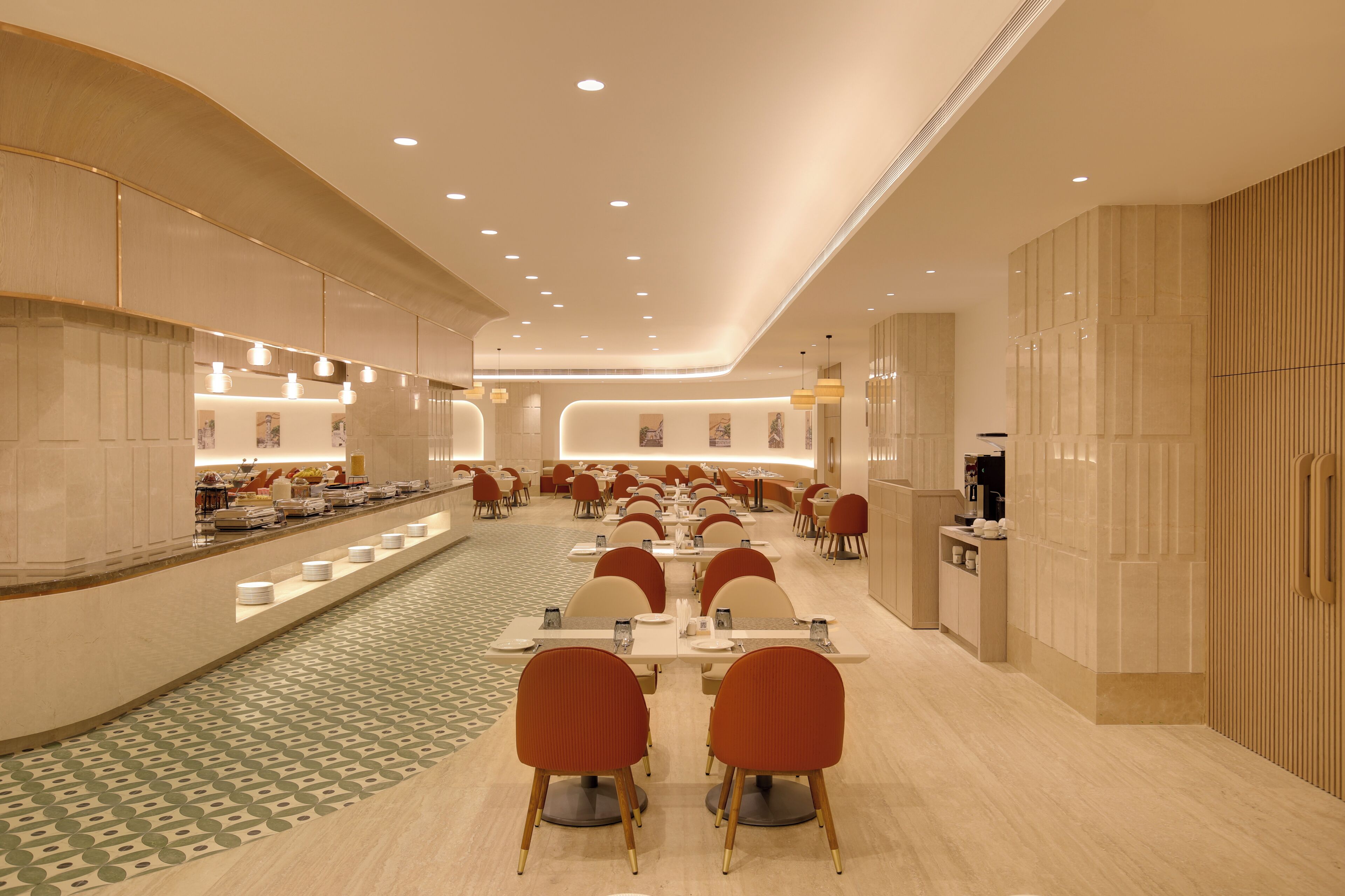 Ein großzügiger Hotel-Speisesaal mit mehreren Tischen und Stühlen, eine Buffettheke links und ein Empfangsbereich rechts.