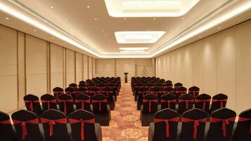 Un salón de conferencias con filas de sillas, cada una adornada con una cinta roja. El salón tiene una alfombra estampada y una lámpara de araña moderna.