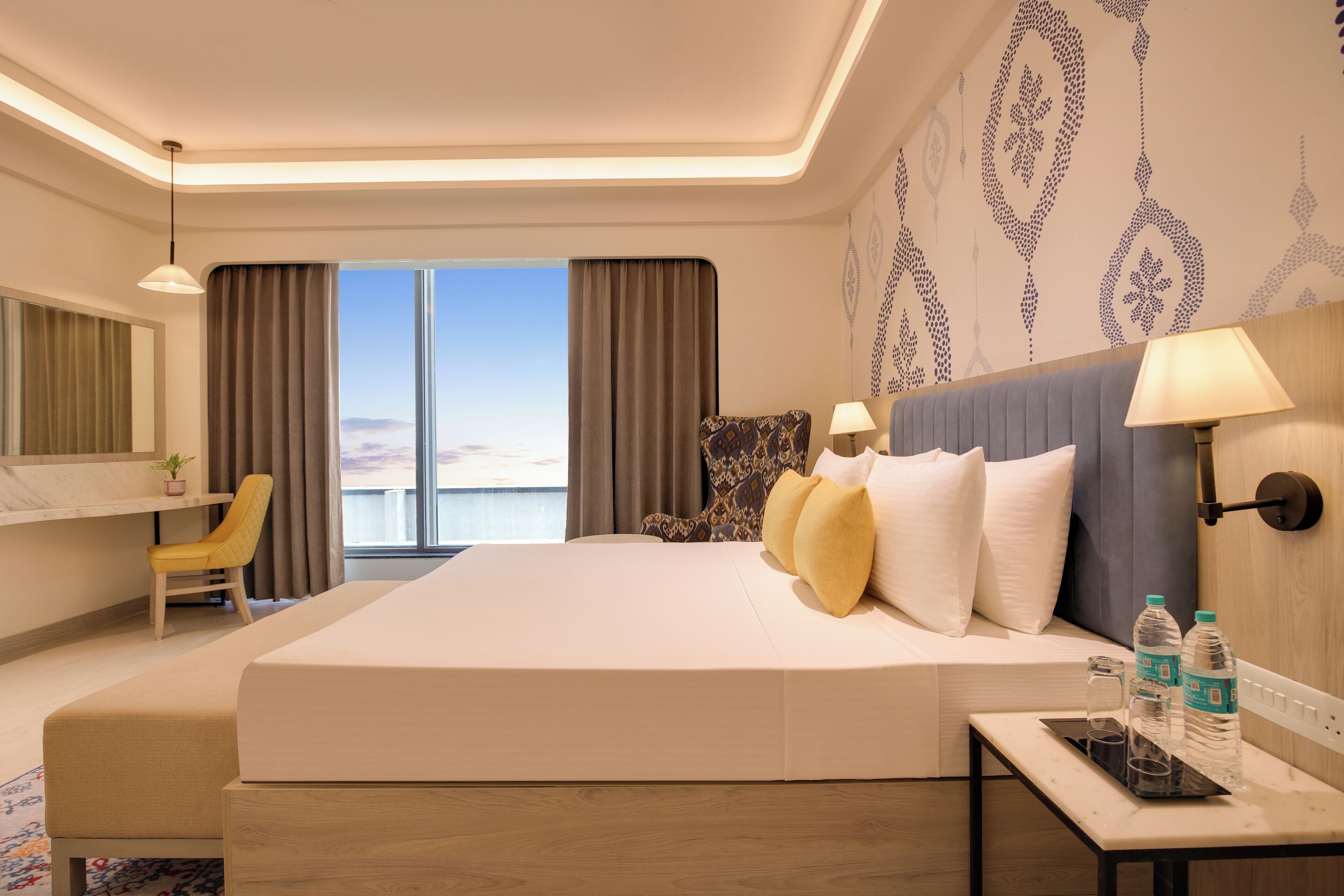 Quarto de hotel com uma cama grande, uma escrivaninha, uma cadeira, uma mesinha de cabeceira e vista para o mar.